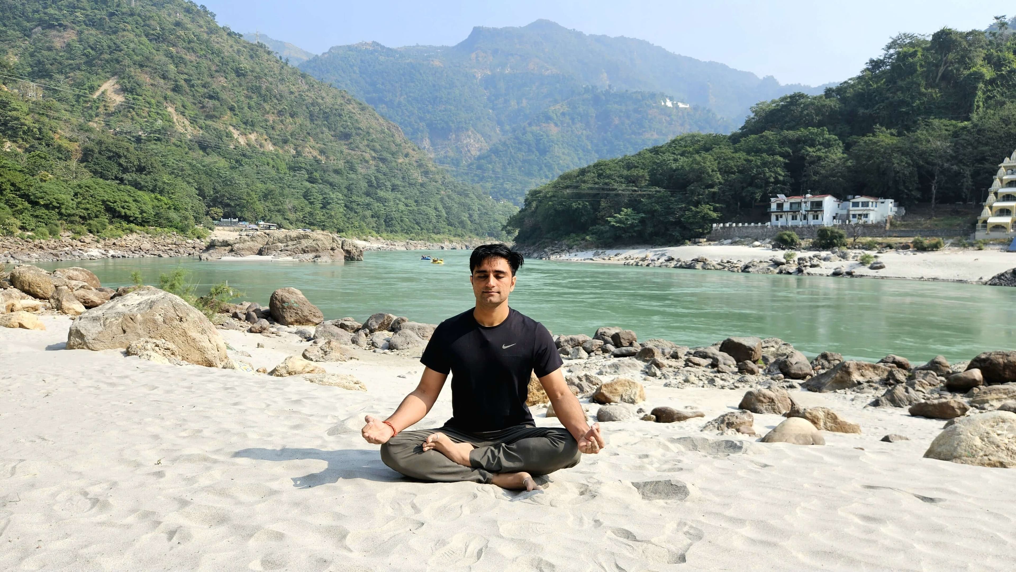 Shubham meditating on a riverbank in the mountains
